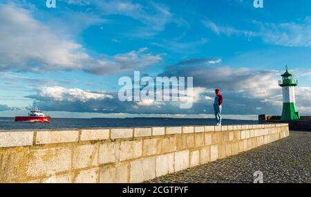 Schöne Landschaft auf der Insel Rügen in der Ostsee am Pier mit einem Leuchtturm und Segelschiff im Hintergrund. Junge Rotschopf Frau zu Fuß Stockfoto