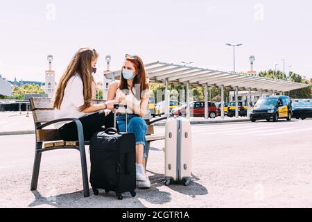 Zwei junge Touristen Frauen sitzen auf einer Bank draußen Der Bahnhof Stockfoto