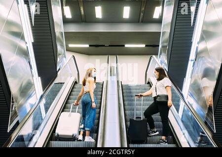 Zwei junge Touristen mit Gesichtsmasken benutzen die U-Bahn-Rolltreppen Stockfoto