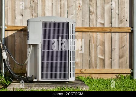 Zentrale Klimaanlage in einem Wohnhinterhof vor einem entkochten Holzzaun und Rasenfläche mit Kopierplatz. Stockfoto