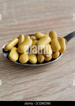 Löffel mit gelben Pillen, Nahrungsergänzungsmittel auf Holztisch. Stockfoto
