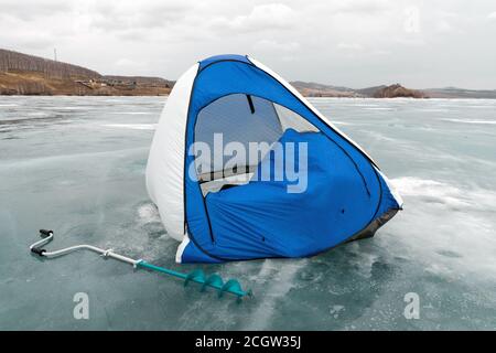 Ein Fischerzelt steht im Wind auf dem schmelzenden Eis des Big Lake gegen das Ufer. Region Krasnojarsk. Russland. Stockfoto