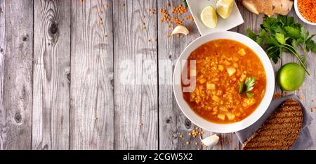 Draufsicht auf vegane rote Linsensuppe mit Zutaten auf grauem Holzhintergrund. Speicherplatz kopieren. Langes Banner. Winter-Food-Konzept Stockfoto