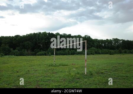 Ländliches Fußballfeld mit leerem und rostigen Torpfosten Vordergrund und Wald im Hintergrund Stockfoto