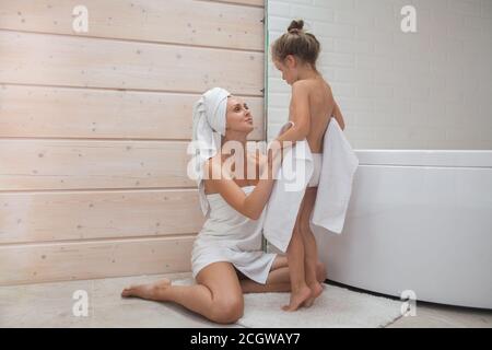 Glückliche liebevolle Familie verbringen Zeit zusammen. Mutter und ihre Tochter Kind Mädchen küssen und umarmen in weißen Badezimmer. Frau und Mädchen mit Handtüchern an Stockfoto