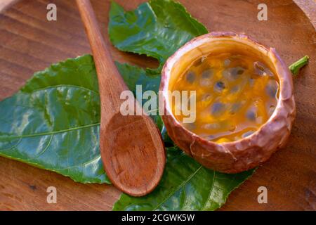 Maracuja in der Hälfte und ganz in kleinen Glasbehälter Schale der Frucht mit Holzlöffel und Blatt auf Teller und weißem Hintergrund geschnitten. Passionsfrucht mit Stockfoto