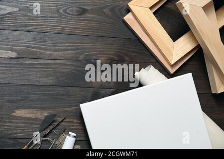 Eine weiße leere Leinwand auf Trage, Palettenmesser, Unterrahmen und ein Rohr mit Ölfarbe auf einem braunen Holztisch liegen. Draufsicht mit Kopierbereich Stockfoto