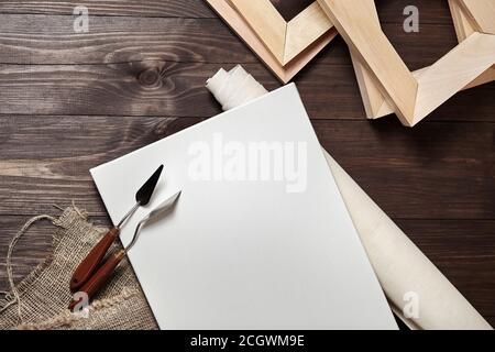 Eine weiße leere rechteckige grundierte Leinwand, Rolle, Palette Messer und Bahren liegen auf einem braunen Holzhintergrund. Draufsicht Stockfoto