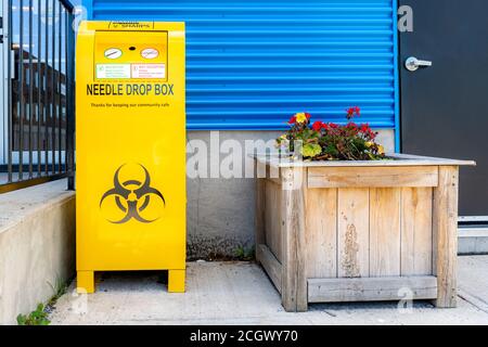 Eine öffentliche Drop-Box für gebrauchte Nadeln, auf einem Bürgersteig bei einem Gebäude. Die Box ist leuchtend gelb und trägt das Standard-Bio-Hazard-Symbol. Stockfoto