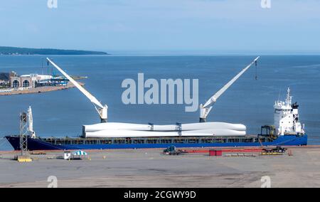 Rotorblätter für eine große Windkraftanlage, die auf einem Schiff geliefert wird. Die Rotorblätter werden auf dem Schiffsdeck gesichert.das Schiff ist mit zwei Kränen ausgestattet. Stockfoto