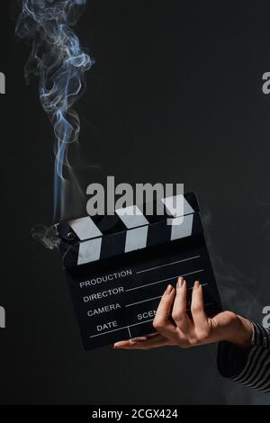 Weibliche Hand hält rauchenden Klapperboard. Rauch kommt aus heißen Film klatschen Board. Stockfoto