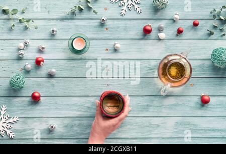 Wintertee, Arrangement mit Glas-Teekanne, Glas Tee in der Hand auf hellblauem minzholzigen Hintergrund. Weihnachtsdekorationen - Spiegelkugeln, Kugel Stockfoto