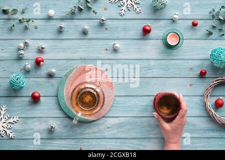 Wintertee, Arrangement mit Glas-Teekanne, Glas Tee in der Hand auf hellblauem minzholzigen Hintergrund. Weihnachtsschmuck, Kugeln, Spielzeug, Tee ca. Stockfoto