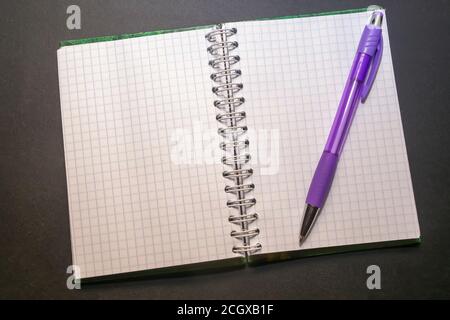 Auf einem schwarzen Tisch liegt Notizblock mit Papier in einem Käfig zusammen mit einem Stift Stockfoto
