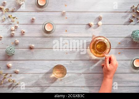 Wintertee, Arrangement mit Glas Teekanne, Glas Tee in der Hand auf hellem, grauem Holzhintergrund. Weihnachtsdekorationen - Spiegelkugeln, Kugeln, zu Stockfoto