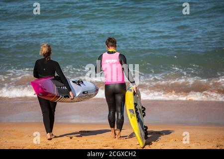 Mann und Frau tragen Neoprenanzüge am Strand mit ihren Surfbrettern, Sydney, Australien Stockfoto