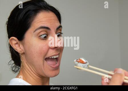 Hübsche Frau isst Brötchen mit Essstäbchen Sushi auf grauem Hintergrund. Japanische Küche. Selektiver Fokus. Japanische Küche. Stockfoto