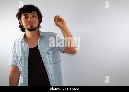 Junger hispanischer gehörloser Mann, der Gebärdensprache verwendet, um zu kommunizieren, auf weißem Hintergrund in legerer Kleidung Stockfoto