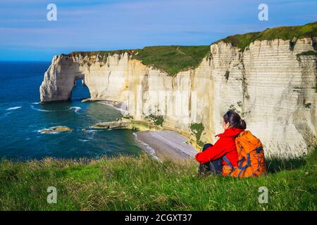 Sorglose glückliche Reisende Frau entspannend und genießen Sie die Aussicht mit Meer. Backpacker Frau sitzt im grünen Gras, Etretat, Normandie, Frankreich, Europa Stockfoto