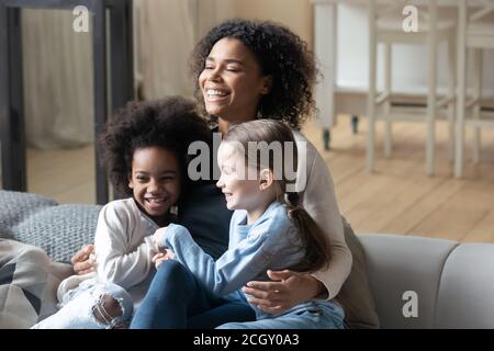 Glückliche junge afroamerikanische Frau kuscheln spielerisch verschiedene Töchter. Stockfoto