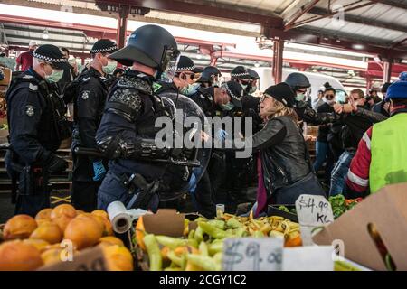 Melbourne, Australien. September 2020. Polizeibeamte der Victoria-Polizei wenden Schilde und Schlagstöcke auf Demonstranten an und drängen sich in die Obst- und Gemüseschuppen auf den Queen Victoria Markets, während eine Protesterin versucht, mit ihnen während eines Anti-Maske- und Anti-Blockdown-Popupproteste in Melbourne Australia zu sprechen. Kredit: Michael Currie/Alamy Live Nachrichten Stockfoto