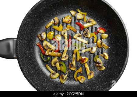 Pilze mit Gemüse in heißem Samenöl in einer Bratpfanne mit Antihaftbeschichtung auf weißem Hintergrund isoliert kochen. Rösten bunte Glocke Stockfoto