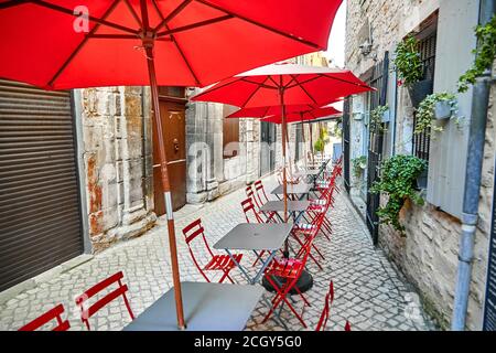 Sommercafé mit roten Sonnenschirmen und Stühlen. Leere graue Tabellen. Draußen ein französisches Touristenrestaurant in der wunderschönen Altstadt. Frankreich, Europa Stockfoto