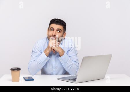 Optimistischer glücklicher Geschäftsmann sitzend Büro-Arbeitsplatz mit Laptop auf dem Schreibtisch, lehnte sich auf die Hände während träumen, Wunschdenken, Gedankendenken inspiriert. ind Stockfoto