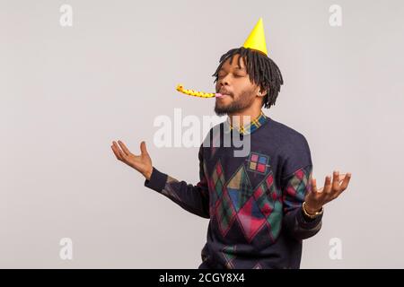 Zufrieden zufrieden afrikanischen Mann mit Dreadlocks in Party Hut Spaß und genießen Blasen Party Horn mit geschlossenen Augen, Geburtstagsfeier. Innen s Stockfoto