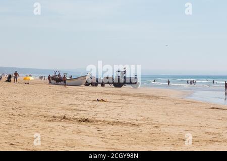 Costa da Caparica, Portugal - 10. September 2020: Eine Kunst der Fischer Schleppnetzfischfang vom touristischen Strand mit einem Traktor. Urlauber beobachten und hellen Stockfoto