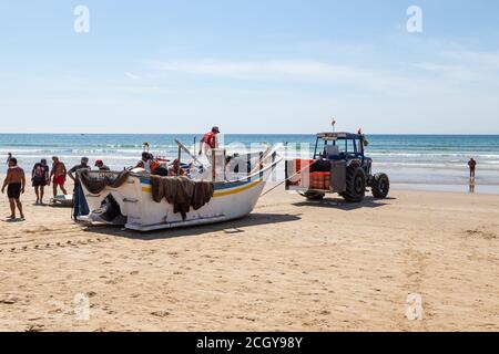 Costa da Caparica, Portugal - 10. September 2020: Eine Kunst der Fischer Schleppnetzfischfang vom touristischen Strand mit einem Traktor. Urlauber beobachten und hellen Stockfoto