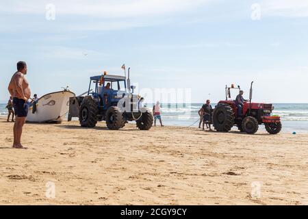 Costa da Caparica, Portugal - 10. September 2020: Eine Kunst der Fischer Schleppnetzfischfang vom touristischen Strand mit einem Traktor. Urlauber beobachten und hellen Stockfoto
