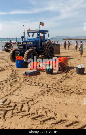 Costa da Caparica, Portugal - 10. September 2020: Eine Kunst der Fischer Schleppnetzfischfang vom touristischen Strand mit einem Traktor. Urlauber beobachten und hellen Stockfoto