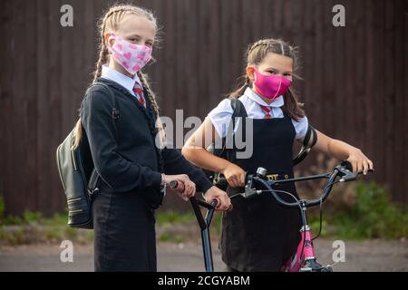 Zwei 10-jährige Schülerinnen in Schuluniform mit ihren Roller und Fahrrad und tragen Gesichtsmasken Stockfoto