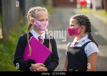Zwei 10-jährige Schülerinnen in Schuluniform und Gesicht Masken stehen draußen und schauen sich an Stockfoto