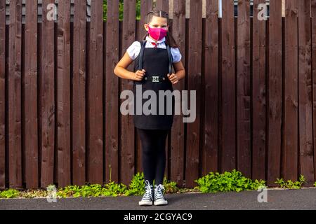 Eine 10-jährige Schülerin trägt eine Schuluniform und rosa Gesichtsmaske und Blick in Richtung Kamera. Stockfoto