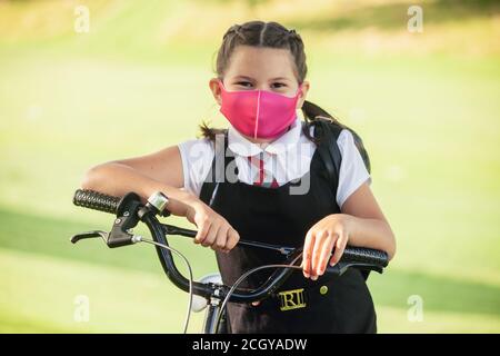 Eine zehnjährige Schülerin, die mit ihren Händen auf ihrem Fahrrad steht und eine Gesichtsmaske trägt. Stockfoto