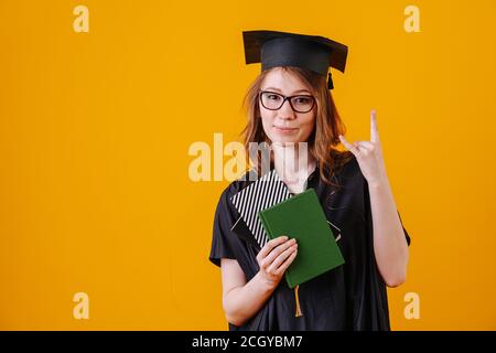 Frau feiert ihren Abschluss, trägt Kleid und Hut. Auf orangefarbenem Hintergrund. Stockfoto
