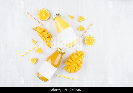 Frischer gelber Orangensaft und Mangosaft in Glasflaschen mit Blankoetikett, Zutaten auf weißem Holzbrett, Mock Up für Design, Werbung, Brandin Stockfoto