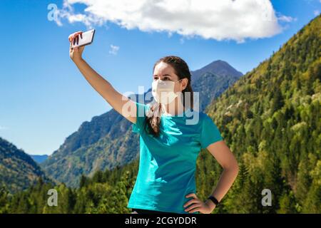 Stock Foto von einer jungen Frau trägt eine Maske und Machen Sie ein Selfie, während Sie einen Tag in den Bergen genießen Und eine schöne Landschaft im Hintergrund Stockfoto