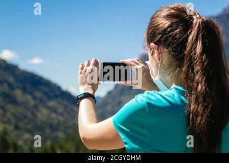 Stock Foto einer Frau von hinten mit Gesichtsmaske Ein Foto von einer schönen Landschaft mit ihrem Handy Stockfoto