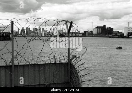 Skyline von London durch eine Metallbarriere gesehen, die vom Thames Path an der Themse, in der Nähe von Woolwich, London, England, aufgenommen wurde Stockfoto