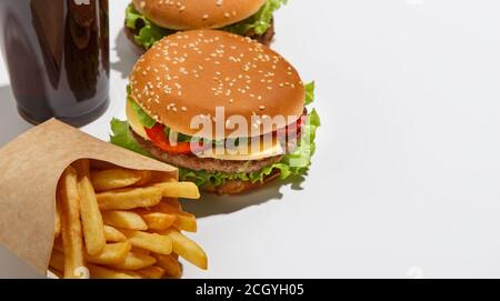 Nach Hause liefern und amerikanische Fast Food zum Mitnehmen. Cheeseburger und Hamburger, pommes Frites in Öko-Packung und ein Glas Cola, isoliert auf weißem Hintergrund Stockfoto