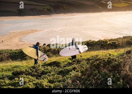 Reife Surfer tragen ihre Surfbretter und laufen eifrig auf einem Fußweg auf dem Pentire Point East in Newquay in Cornwall. Stockfoto