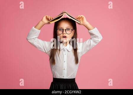 Überrascht Grundschule Mädchen in Brille bedeckt ihren Kopf mit Buchen Stockfoto