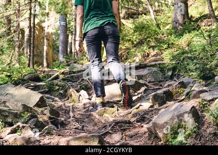 Nahaufnahme Beine in Sport-Trekkingschuhe auf grünem Gras und felsigen Steinen mit Moos von Berg Herbst Wald. Frau klettert in sportlicher Kleidung und Rucksack Stockfoto