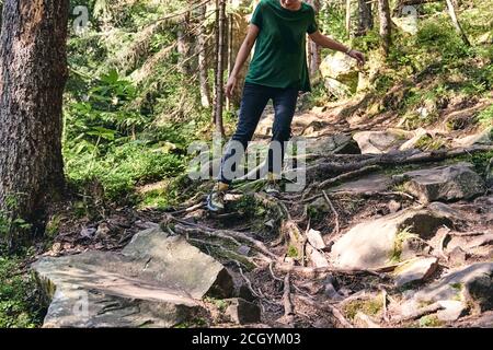 Nahaufnahme Beine in Sport-Trekkingschuhe auf grünem Gras und felsigen Steinen mit Moos von Berg Herbst Wald. Frau klettert in sportlicher Kleidung und Rucksack Stockfoto