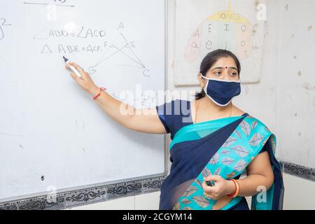 Weibliche Lehrerin Tragen Maske und lehren zeigen auf Whiteboard im Klassenzimmer, indische Schulklasse während covid19 Pandemie, neue Normalität Stockfoto