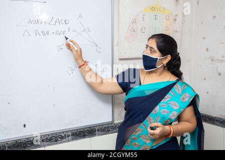 Weibliche Lehrerin Tragen Maske und Saree lehren Mathematik auf Whiteboard im Klassenzimmer, indische Schulklasse während covid19 Pandemie, neue Normalität Stockfoto