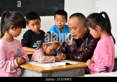 (200913) -- RONGJIANG, 13. September 2020 (Xinhua) -- Gun Luquan hilft Schülern bei Hausaufgaben an der Miaoben Grundschule in Zhongcheng Township, Bezirk Rongjiang, südwestlich von Chinas Provinz Guizhou, 8. September 2020. Gun Luquan und seine Frau Pan Mingzhen sind ein Lehrerpaar, das sich seit mehr als 20 Jahren ländlichen Schülern der Miaoben Grundschule im bergigen Bezirk Rongjiang widmete. Da die Schule nur noch zwei Lehrende Mitglieder, Gun und Pan haben nie aufgegeben ihre ursprüngliche Verfolgung und ihr Bestes versucht, um den Schülern eine anständige Schulerfahrung zu bieten. (Xinhua/Yang Wenbin) Stockfoto